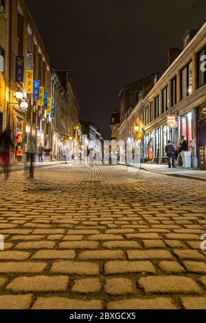 MONTREAL, KANADA - 17. MAI 2015: Gebäude und Geschäfte entlang der Rue Saint Paul in der Altstadt von Montreal bei Nacht. Die Unschärfe der Menschen ist zu sehen. Stockfoto