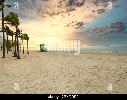 Dramatischer Sonnenaufgang am Strand mit Palmen und Rettungsschwimmer Turm Stockfoto
