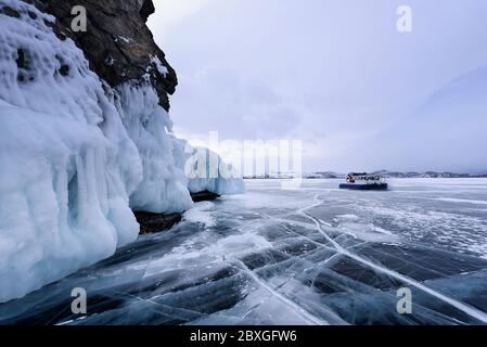 Die Menschen reisen auf dem Eis des zugefrorenen Baikalsees in einem sicheren und komfortablen Hovercraft. März in der Nähe eines mit Eis bedeckten Felsens Stockfoto