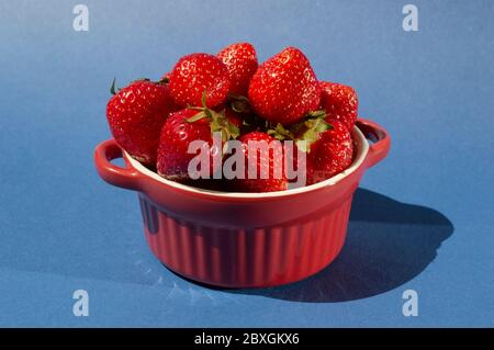 Eine Gruppe von frischen köstlichen Erdbeeren in roten Zementplatte mit Griffen. Helle kreative Keramik Konzept. Art trendy saisonalen Sommerobst Stockfoto