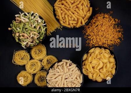 Rohe runde Pasta auf dunklem Hintergrund. Das Wort PASTA aus Holzbuchstaben in der Mitte. Das Konzept der köstlichen Speisen. Draufsicht, flaches Layout, Kopie Stockfoto