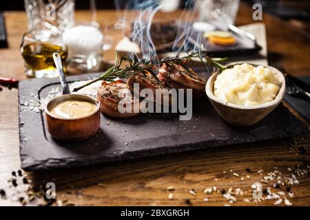 Schweinelende mit pürierten Kartoffeln, Speck und Senfsoße mit Zweig rauchenden Rosmarin. Köstliche gesunde traditionelle gegrillte Fleischgerichte serviert Stockfoto