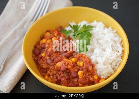 Chili con Carne mit langkörnigem Reis, der mit einem Blatt Petersilie-Nahaufnahme verziert ist Stockfoto