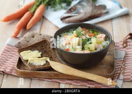 Finnische cremige Lachssuppe Lohikeitto auf einem Holztablett mit Roggenbrot, Butter und Grüns serviert Stockfoto