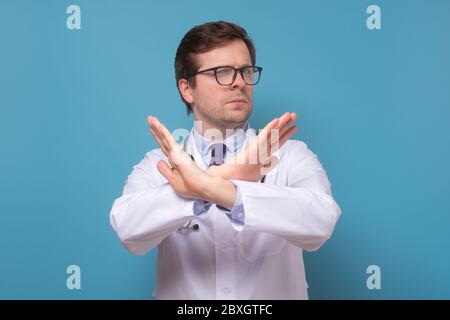Ernst kaukasischen männlichen Arzt, Kreuz mit den Händen über der Brust, zeigt Stop-und Prohibition-Geste, etwas ablehnen, nein sagen. Soziale Distanc Stockfoto