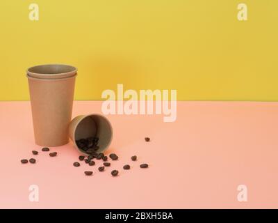 Pappbecher und Kaffeebohnen auf rosa und gelbem Hintergrund. Einweggeschirr für Kaffee, Tee und andere Getränke. Stockfoto