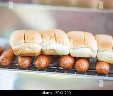 Mehrere Hot Dogs auf einem Grill mit Brötchen auf dem Dach. Nahaufnahme Stockfoto