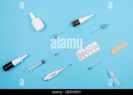 Medikamente zur Behandlung von Erkältungen auf blauem Hintergrund. Pillen und Pillenflaschen, Spritzen und Thermometer. Stockfoto