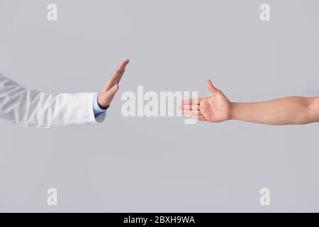 Arzt weigert sich, die Hand des Patienten auf hellem Hintergrund zu schütteln. Konzept der sozialen Distanz Stockfoto