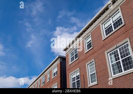 Der Blick auf zwei braune Backsteingebäude mit mehreren geschlossenen Doppelhangfenstern mit weißer Verkleidung im obersten Stockwerk. Blauer Himmel und Wolken sind im Hintergrund. Stockfoto