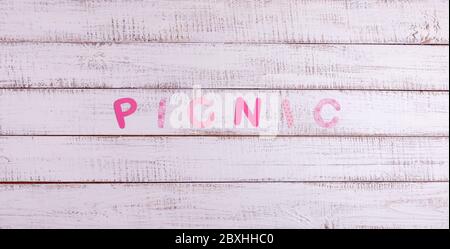 Auf einem hölzernen Hintergrund ist das Wort Picknick aus Papierbuchstaben. Blick von oben. Stockfoto