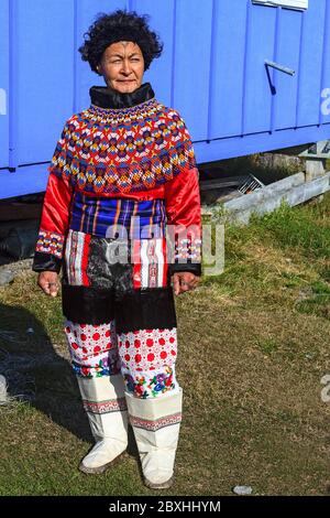 Inuit Frauen in traditioneller grönländischer Kleidung, die stark mit Perlen verziert sind und vor einem typischen bunten Dorfhaus stehen Stockfoto