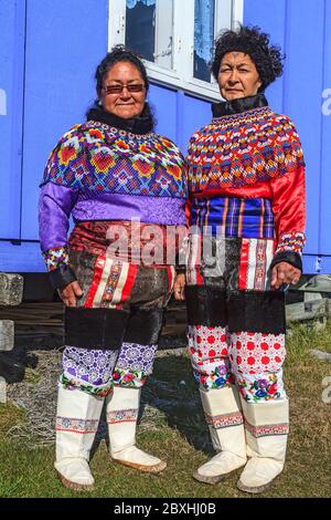 Inuit Frauen in traditioneller grönländischer Kleidung, die stark mit Perlen verziert sind und vor einem typischen bunten Dorfhaus stehen Stockfoto