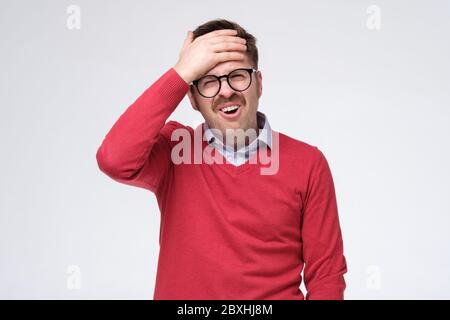 Erschöpft fühlen. Junger Mann in rotem Pullover mit dem Kopf und der Temperatur. Studioaufnahme. Stockfoto