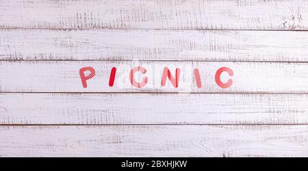Auf einem hölzernen Hintergrund ist das Wort Picknick aus Papierbuchstaben. Blick von oben. Stockfoto
