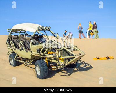 ICA, PERU - 6. JULI 2010: Sanddünenbuggy auf einer Düne geparkt und eine Gruppe von Menschen, die Spaß haben. Ica, Peru. Stockfoto