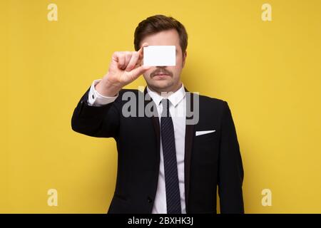 Kaukasischer Mann in Anzug zeigt Visitenkarte geben eine perfekte oder ok Geste. Studio auf gelber Wand gedreht. Stockfoto