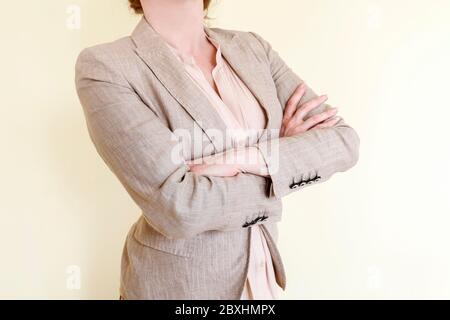 Frau in eleganten Anzug steht mit verschränkten Armen. Körpersprache, selbstbewusste Person. Stockfoto