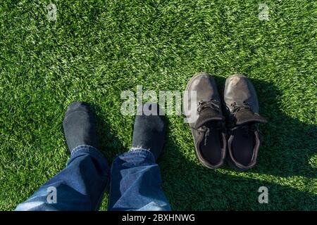Die Beine eines Arbeiters ohne Schuhe auf dem Fußballplatz. Der Mann zog seine Schuhe aus und stand in Socken auf dem Fußballplatz. Grünes Gras und weißer Rand li Stockfoto
