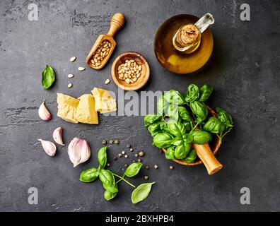 Pesto-Sauce Kochen. Basilikumblätter, Olivenöl, Knoblauch, Pinienkerne und Parmesan. Blick von oben auf den dunklen Steintisch Stockfoto