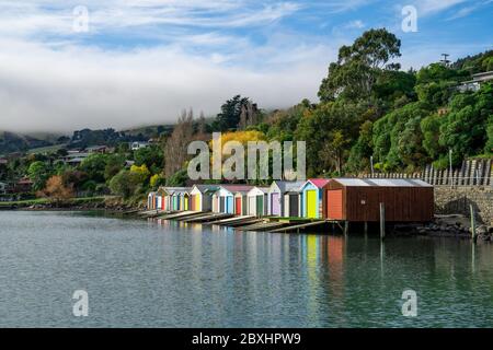 Bunte Bootsschuppen mit schönen Reflektionen am Tag in Duvauchelle, Akaroa Hafen auf Banks Peninsula in South Island, Neuseeland. Stockfoto