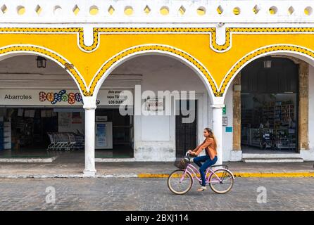 Junge mexikanische Frau auf einem Fahrrad mit Unschärfe-Bewegung in der gelben Stadt Izamal mit Bogenarchitektur am Hauptplatz, Yucatan Halbinsel, Mexiko. Stockfoto