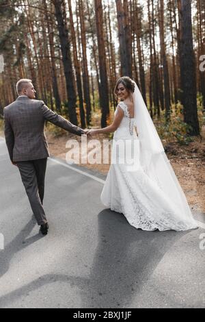 Braut und Bräutigam gehen auf der Straße im Wald von hinten fotografiert. Porträt von Braut und Bräutigam Stockfoto