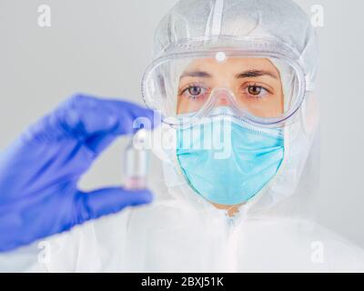 Arzt mit Gesichtsmaske, Schutzbrille und PSA-Anzug für Coronavirus (Covid-19), der Covid-19-Impfstoff auf weißem Hintergrund hält, Covid-19 q Stockfoto