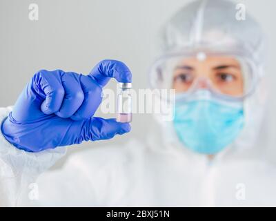 Arzt mit Gesichtsmaske, Schutzbrille und PSA-Anzug für Coronavirus (Covid-19), der Covid-19-Impfstoff auf weißem Hintergrund hält, Covid-19 q Stockfoto