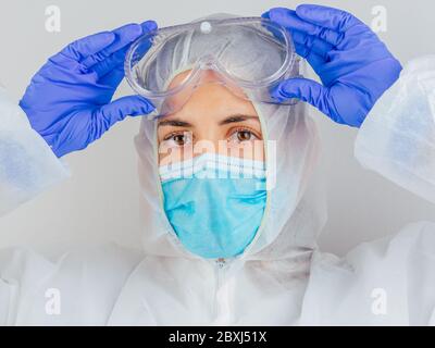 Junge Ärztin in Uniform, medizinische Kappe und Maske, Nahaufnahme Porträt. Sie legt die Brille. Coronavirus-Konzept. Stockfoto