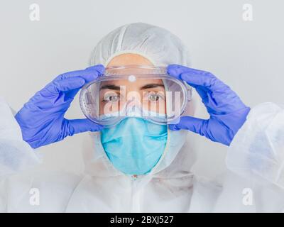 Junge Ärztin in Uniform, medizinische Kappe und Maske, Nahaufnahme Porträt. Sie legt die Brille. Coronavirus-Konzept. Stockfoto