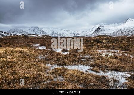 Winter schottische Highlands Landschaft mit stürmischem Himmel. Schneebedeckte Gipfel der Black Mount Range über die Lochans von Rannoch Moor. Stockfoto