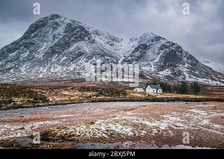 Malerische Winterlandschaft von Glen Coe mit dem ikonischen weißen Häuschen vor der Kulisse des Buachaille Etive Mor und stürmischen Wolken am Horizont. Stockfoto