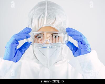 Junge Ärztin in Uniform, medizinische Kappe und Maske, Nahaufnahme Porträt. Sie legt die Brille. Coronavirus-Konzept. Stockfoto