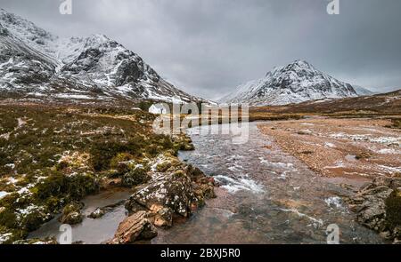 Malerische Winterlandschaft von Glen Coe mit dem ikonischen weißen Häuschen vor der Kulisse des Buachaille Etive Mor und stürmischen Wolken am Horizont. Stockfoto