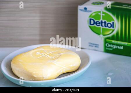 Nahaufnahme des antibakteriellen Dettol Seifenstegs auf einem blauen Seifenhalter auf einem Waschbecken im Bad mit der Schachtel mit Dettol-Logo im Hintergrund. Stockfoto