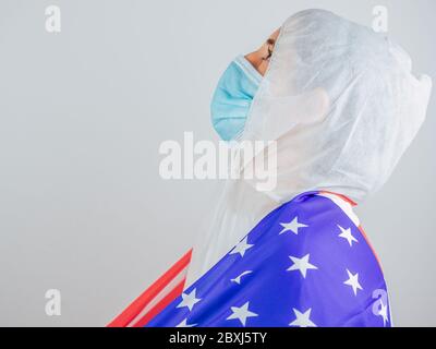 Porträt einer kaukasischen Ärztin mit psa-Anzug und Maske im Krankenhaus. Hält die Flagge der Vereinigten Staaten. Frau vor dem Coronavirus geschützt. Stockfoto