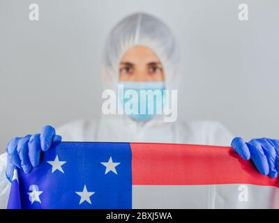 Porträt einer kaukasischen Ärztin mit psa-Anzug und Maske im Krankenhaus. Hält die Flagge der Vereinigten Staaten. Frau vor dem Coronavirus geschützt. Stockfoto