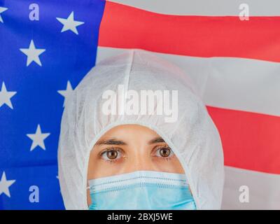 Porträt einer kaukasischen Ärztin mit psa-Anzug und Maske im Krankenhaus. Hält die Flagge der Vereinigten Staaten. Frau vor dem Coronavirus geschützt. Stockfoto