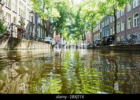 Mann auf einem SUP (Stand-up Paddle Board) auf den Kanälen im Zentrum von Quiet Amsterdam (Niederlande) während der Covid-19-Krise Stockfoto