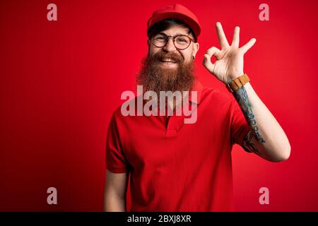 Junge schöne Lieferung Mann trägt Brille und rote Kappe über isolierten Hintergrund lächelnd positiv tun ok Zeichen mit Hand und Finger. Erfolgreiche Ausg Stockfoto