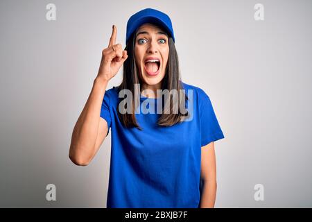 Junge Lieferfrau mit blauen Augen trägt Kappe über blauem Hintergrund mit Finger nach oben mit erfolgreicher Idee stehend. Verlassen und glücklich. Nummer eins. Stockfoto