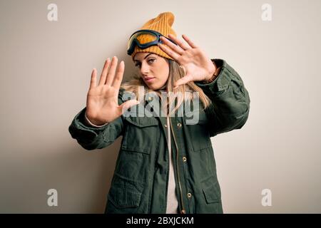 Junge Brünette Skifahrer Frau trägt Schnee Kleidung und Skibrille auf weißem Hintergrund tun Rahmen mit Händen Handflächen und Finger, Kameraperspektive Stockfoto