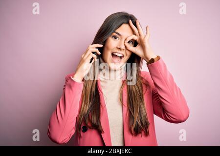 Junge schöne Mädchen mit Gespräch sprechen auf dem Smartphone auf weißem Hintergrund mit glücklichem Gesicht lächelnd tun ok Zeichen mit Hand auf Auge schauend Stockfoto