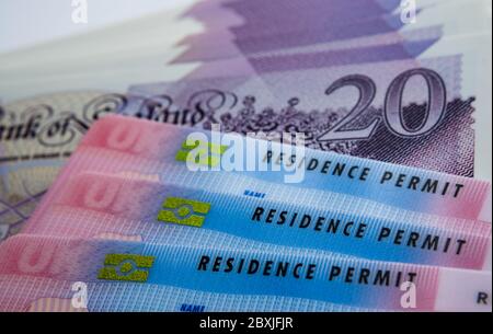 UK biometrische Aufenthaltstitel und 20 Pfund Banknoten. BRP-Karten für Tier 2 Arbeit Visum Einwanderer freigegeben. Konzept Bild für den Preis des Visums. Stockfoto