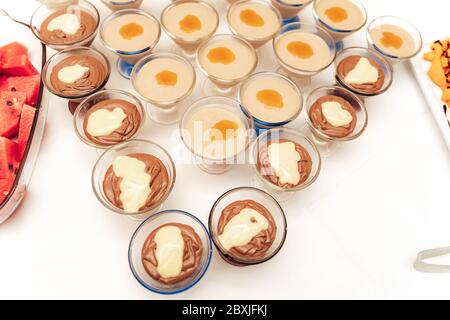 Draufsicht auf Gläser Reihen mit süßen Vanille, Schokolade oder Obst Dessert auf weißem Tisch. Selbstbedienungsbuffet. Feier, Party, Hochzeit Stockfoto