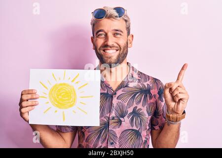 Schöner blonder Tourist Mann im Urlaub trägt Sonnenbrille mit Papier halten mit Sonne zeichnen lächelnd glücklich mit Hand und Finger zur Seite zeigen Stockfoto