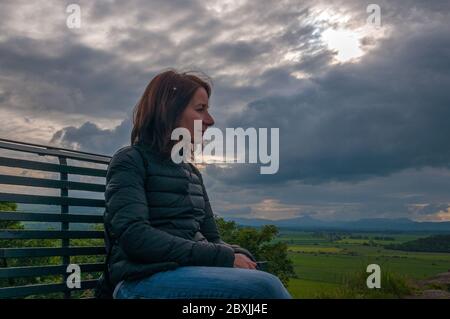 Mädchen sitzt auf einer Bank, während nachdenklich die Landschaft Stockfoto