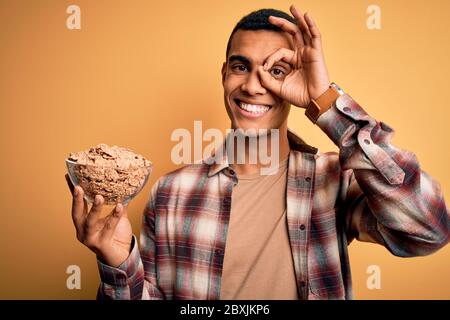 Junge gut aussehende afroamerikanischen Mann hält Schüssel mit gesunden Cornflakes Getreide mit glücklichen Gesicht lächelnd tun ok Zeichen mit Hand auf Auge suchen thrug Stockfoto