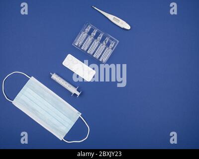 Maske, Spritze, Thermometer, Tabletten und Kapseln auf blauem Hintergrund. Stockfoto